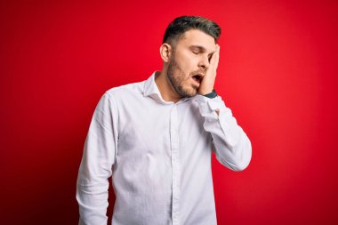 Mavi gözlü, zarif gömlekli genç bir iş adamı kırmızı izole edilmiş arka planda duruyor. Yüzünün yarısını, gözünü ve ağzını eliyle kapatmaktan yoruluyor. Yüzüm acıyor..