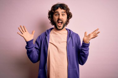 Genç yakışıklı, sakallı, pembe arka planda rahat bir eşofman giyen çılgın ve başarıyı kollarını kaldırıp heyecanla bağırarak kutlayan yakışıklı bir adam. Kazanan konsept