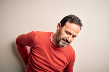 Orta yaşlı, turuncu bir süveter giyen, izole edilmiş beyaz arka planda duran sırt ağrısı çeken, elle dokunan, kas ağrısı çeken bir adam.