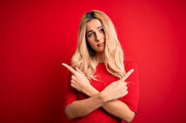 Ayrı kırmızı arka planda dikilen, gündelik tişört giyen genç, güzel sarışın kadın iki tarafı da parmaklarıyla işaret ediyor. Farklı yönler farklı.