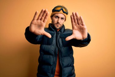 Kar giysileri ve kayak gözlüğü takan sakallı yakışıklı kayakçı elleri ve parmakları kullanarak çerçeve yapıyor.