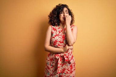 Genç, güzel, kıvırcık Arap kadın tatilde. Çiçekli bir elbise ve güneş gözlüğü takıyor. Elleri ağızdan tırnak yerken gergin ve stresli görünüyor. Endişe sorunu.