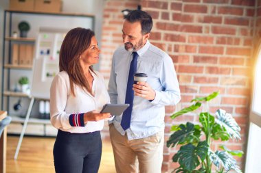 Mutlu ve kendinden emin gülümseyen iki orta yaşlı iş adamı. Birlikte çalışmak, gülümsemek, tablet kullanmak, ofiste kahve içmek.