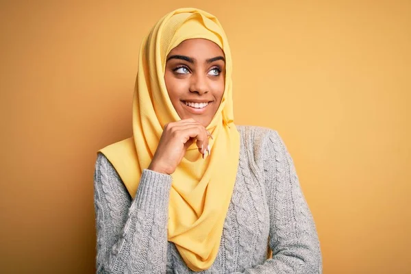 孤立した黄色の背景の上にイスラム教徒のヒジャーブを身に着けている若い美しいアフリカ系アメリカ人の少女 笑顔と思慮深い顔 疑いの概念 — ストック写真