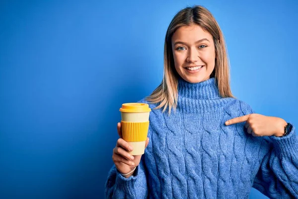 若いです美しいです女性ホールド取りますコーヒーのガラス以上隔離された青の背景とともに驚き顔指差し指に彼自身 — ストック写真