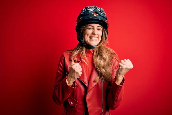 腕を上げて成功のために興奮した赤の背景に元ヘルメットを身に着けている若い美しいブルネットのオートバイの女性と目は勝利笑顔を祝う閉じました 勝者のコンセプト — ストック写真