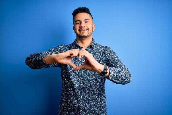 Young handsome man wearing casual shirt standing over isolated blue background smiling in love doing heart symbol shape with hands. Romantic concept.
