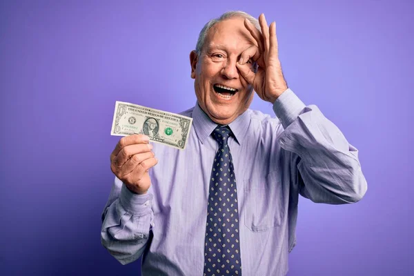 Senior Siwowłosy Mężczyzna Trzymając Jeden Dolar Banknot Fioletowym Tle Uśmiechem — Zdjęcie stockowe