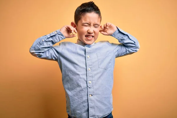 黄色の隔絶された背景にエレガントなシャツを着た若い男の子が 大きな音楽のノイズに悩まされている表情で耳を覆います ろう者の概念 — ストック写真