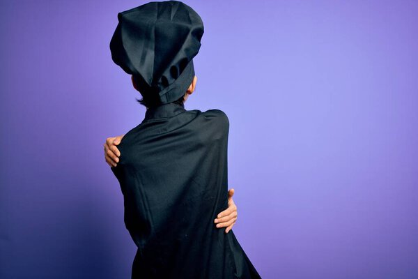 Молодая красивая китайская шеф-повар женщина в форме плита и шляпа на фиолетовом фоне обнимая себя счастливым и положительным из задом наперёд. Самолюбие и забота о себе
