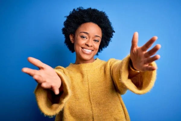 カメラを見て黄色のカジュアルなセーターを着て巻き毛を持つ若い美しいアフリカ系アメリカ人アフロ女性は抱擁のために腕を開いて笑顔 幸せを受け入れる陽気な表情 — ストック写真