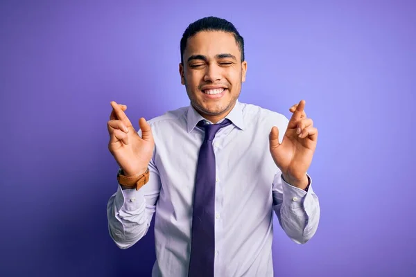 孤立した紫色の背景の上に立つエレガントなネクタイを身に着けている若いブラジルのビジネスマンは 指をジェスチャー希望と目を閉じて笑顔を越えました 幸運と迷信の概念 — ストック写真