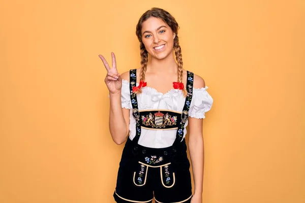 青い目をした若い美しいブロンドのドイツ人女性は 勝利のサインを行う指を示すカメラを見て笑顔伝統的な10月祭のドレスを着ています 第二番 — ストック写真