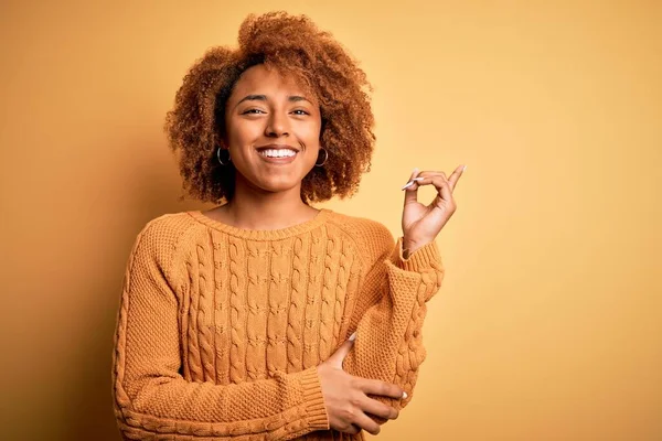 若いです美しいですアフリカ系アメリカ人アフロ女性とともに巻き毛を身に着けていますカジュアルなセーターで顔に大きな笑顔 カメラを見ている側に手と指で指して — ストック写真