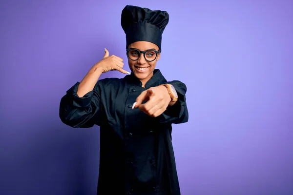 年轻的非洲女厨师身穿炊具制服 头戴紫色背景的帽子 微笑着在电话上说话 指着你 打给我 — 图库照片