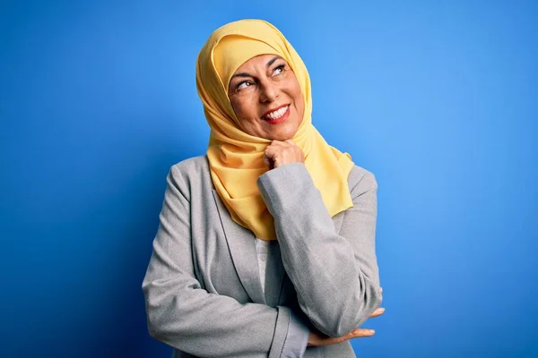 中世のブルネットのビジネス女性は 集中的な表現について考える顎の手で青の背景にイスラム教徒の伝統的なヒジャーブを身に着けています 笑顔と思慮深い顔 疑いの概念 — ストック写真