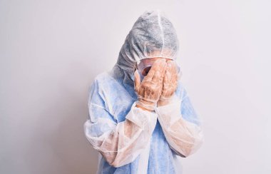 Beyaz arka planda koruyucu koronavirüs ekipmanı takan orta yaşlı bir hemşire. Ağlarken yüzünü ellerle kapatan üzgün bir ifade. Depresyon kavramı.