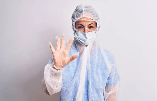 白い背景の上に保護コロナウイルス装置を身に着けている中年の看護師の女性が現れ 自信と幸せ笑顔ながら指番号5で指摘 — ストック写真