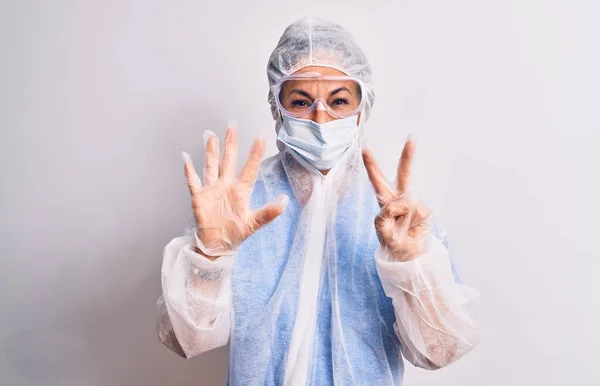 白い背景の上に保護コロナウイルス装置を身に着けている中年の看護師の女性が現れ 自信と幸せ笑顔ながら指番号7で指摘 — ストック写真