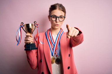 Pembe arka planda madalyalar takan genç, güzel, kızıl saçlı kadın kamerayı işaret ediyor ve sen, el işareti, ön taraftan pozitif ve kendinden emin bir hareket.