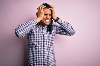 Başı ağrıyan ve acı ve migren yüzünden stres altında olan, rastalı tişörtlü Afro-Amerikan genç yakışıklı adam. Ellerini başının üstüne koy..