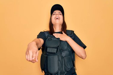Genç, güzel, esmer, polis üniforması giyen, kurşun geçirmez ve şapkalı bir kadın. Sana gülüyor, eli vücudunun üzerinde kamerayı işaret ediyor. Utanç ifadesi.