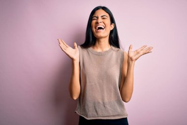 Pembe arka plan üzerine süveter giyen genç ve güzel İspanyol moda kadını kollarını kaldırmış ve gözlerini kapatmış heyecanla haykırarak başarının çılgınlığını kutluyor. Kazanan konsept