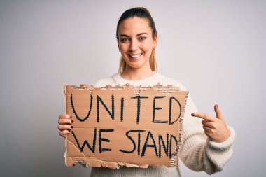 Mavi gözlü, genç ve güzel sarışın kadın birleşik ayakta durup bayrağı tutarak mutlu bir şekilde elini ve parmağını işaret ediyor.
