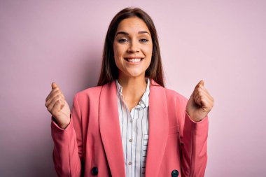 İzole edilmiş pembe arka plan üzerinde duran genç, güzel esmer kadın kollarını kaldırarak ve açık gözlerle başarıyı kutluyor ve şaşırıyor. Kazanan konsept.