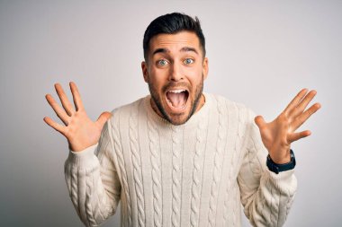 İzole edilmiş beyaz arka planda dikilmiş, kollarını kaldırıp heyecanla haykıran, çılgın ve başarıyı kutlayan genç, yakışıklı bir adam. Kazanan konsept