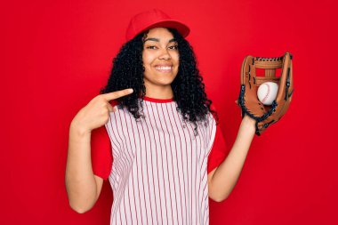 Genç Afro-Amerikan kıvırcık saçlı, kep takan, beyzbol oynayan, top ve eldiven takan, sürpriz yüzlü, kendini gösteren.