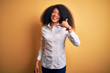 Afro saçlı, sarı arka planda gülümseyen, el ve parmaklarıyla telefonla konuşan güzel Afro-Amerikan zarif kadını. İletişim kavramları.