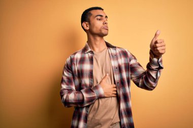 Sarı arka planda dikilen, gururlu, gülümseyen, sıradan bir tişört giyen genç Afrikalı Amerikalı.