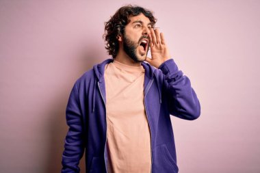 Genç, yakışıklı, sakallı, pembe arka planda sıradan bir kazak giyen, el ele tutuşarak bağıran ve yüksek sesle bağıran bir adam. İletişim konsepti.