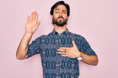 Yakışıklı İspanyol bohem bir adam pembe arka plan üzerinde hippi tarzı giyinmiş göğsü ve avucu açık yemin ederek sadakat yemini ediyor.