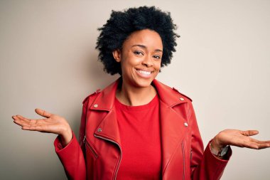 Young beautiful African American afro woman with curly hair wearing casual red jacket clueless and confused expression with arms and hands raised. Doubt concept. clipart