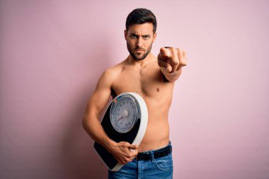 Pembe arka planda sakalsız, sakalsız, genç, yakışıklı, zayıf adam kamerayı işaret ediyor ve sen, el işareti, ön taraftan pozitif ve kendinden emin bir hareket.