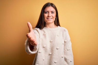 Mavi gözlü, sıradan bir süveter giyen, sarı arka planda duran genç ve güzel bir kadın selamlaşma ve dostça bir selamlama olarak el sıkışma sunuyor. Başarılı bir iş..