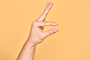 İzole edilmiş sarı arka plan üzerinde parmaklarını gösteren beyaz bir adamın eli. Görünmez bir şeyi alıp, parmaklarıyla uzayı gösteren bir nesneyi tutuyor.