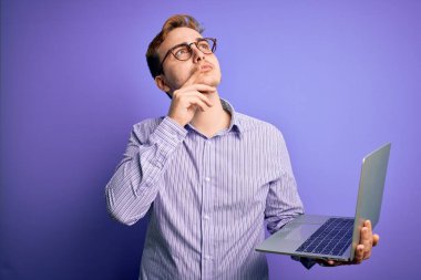 Genç, kızıl saçlı, laptopla çalışan bir iş adamı. Mor arka plan üzerinde çalışıyor. Ciddi bir yüz.
