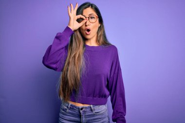 Mor izole edilmiş arka planda gözlük takan genç ve güzel bir kadın. Şaşırmış yüz ifadesiyle şaşırmış, parmaklarından bakan gözler. İnançsız ifade.