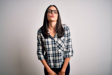 Mavi gözlü, sıradan gömlekli, beyaz arka planda gözlüklü genç esmer bir kadın havada öpüşürken kameraya bakıyor. Güzel ve seksi. Aşk ifadesi.