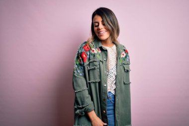 Moda kıyafetleri giyen genç ve güzel bir kadın. Manken, sokak tarzı giyiniyor. Pembe arka planda dikiliyor.