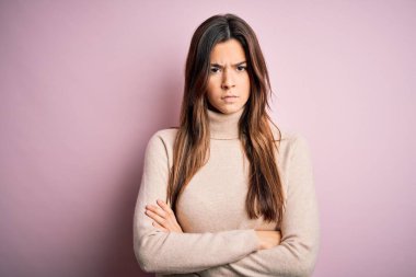 Balıkçı yaka kazak giyen genç ve güzel bir kız pembe arka plan üzerinde duruyor şüpheci ve gergin, yüzünde çapraz kollu tasvip etmeyen bir ifade. Negatif kişi.