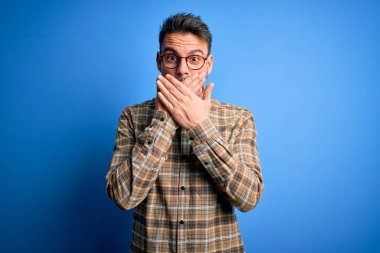 Mavi arka planda duran sıradan gömlek ve gözlük takan genç yakışıklı adam yanlışlıkla ağızlarını kapatarak şok geçirdi. Gizli konsept.