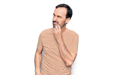 Orta yaşlı, çizgili tişört giyen yakışıklı bir adam izole edilmiş beyaz arka planda dikilirken parmak çenesinde şüpheye yoğunlaşır ve yukarı bakar.