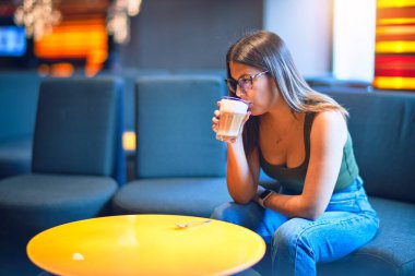 Young beautiful woman drinking glass of coffee sitting at restaurant