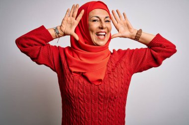 Orta yaşlı esmer kadın izole edilmiş beyaz arka plan üzerine geleneksel tesettür takmış neşeli gülümseyen, elleri havada bir böceği dikizleyen. Şaşırdım ve çıktım.