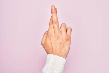 İzole edilmiş pembe arka plan üzerinde parmaklarını gösteren beyaz bir gencin eli. Parmakları çapraz, batıl inançlar ve şanslı bir jest, şanslı ve umut dolu bir ifade.