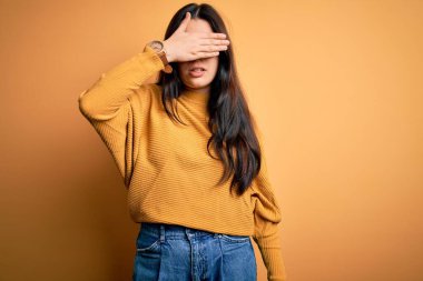 Genç esmer kadın gözlük takıyor ve sarı izole edilmiş arka plan üzerine gündelik süveter giyiyor gözleri elle kaplıyor, ciddi ve üzgün görünüyor. Görme, saklama ve reddetme konsepti